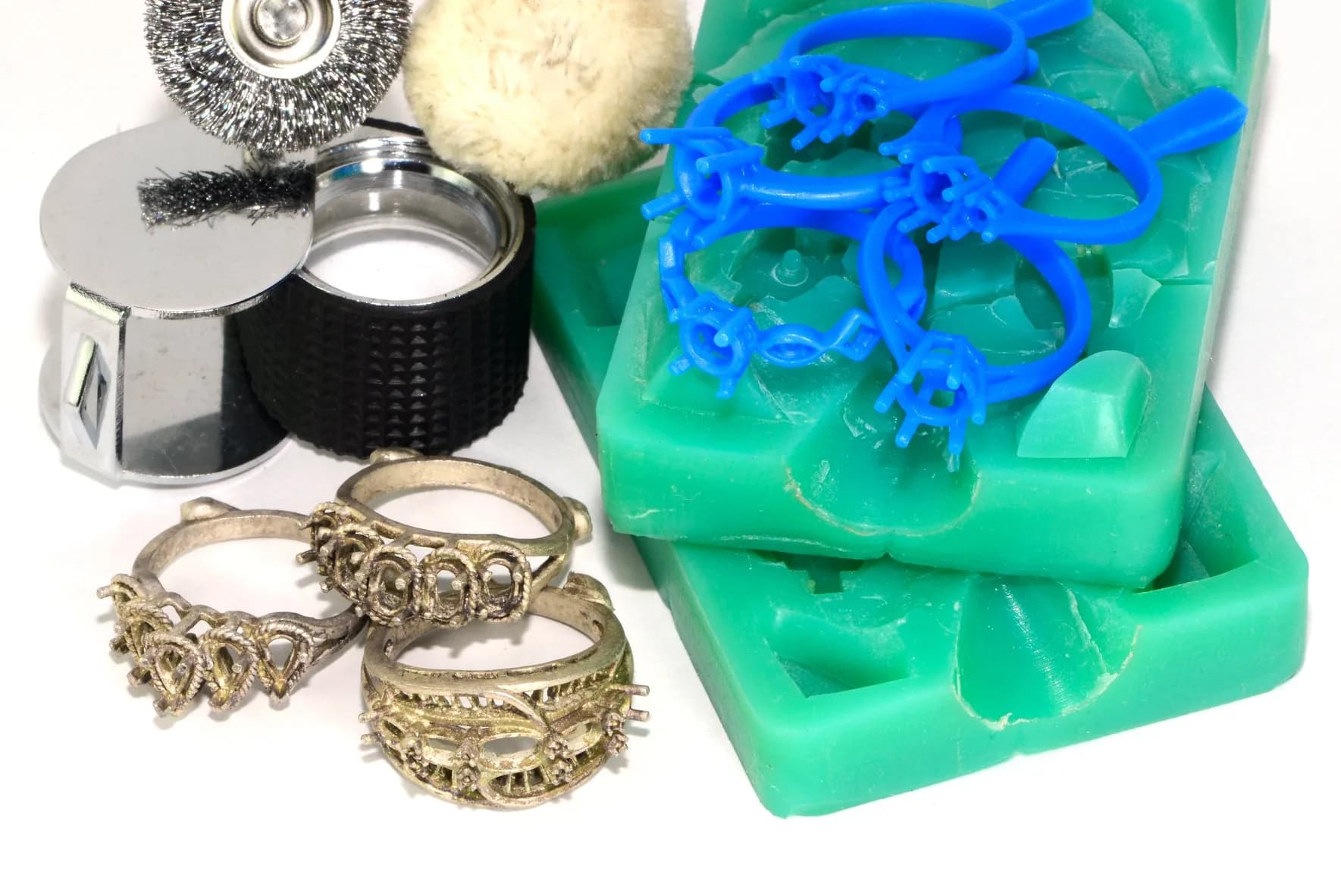 Green RTV silicone moulds with blue wax injections and cast ring blanks alongside finishing tools