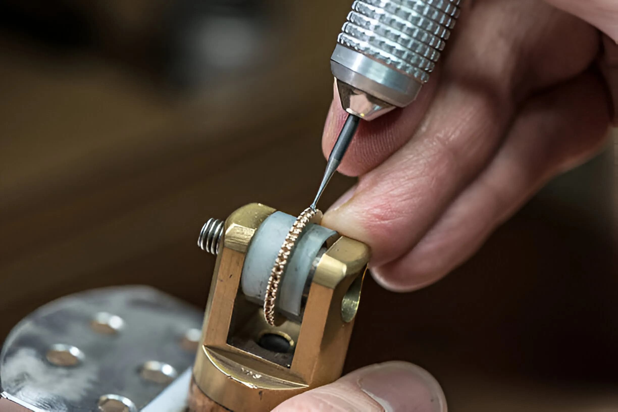 Jewellery artisan setting diamonds into a gold ring held in a vice clamp