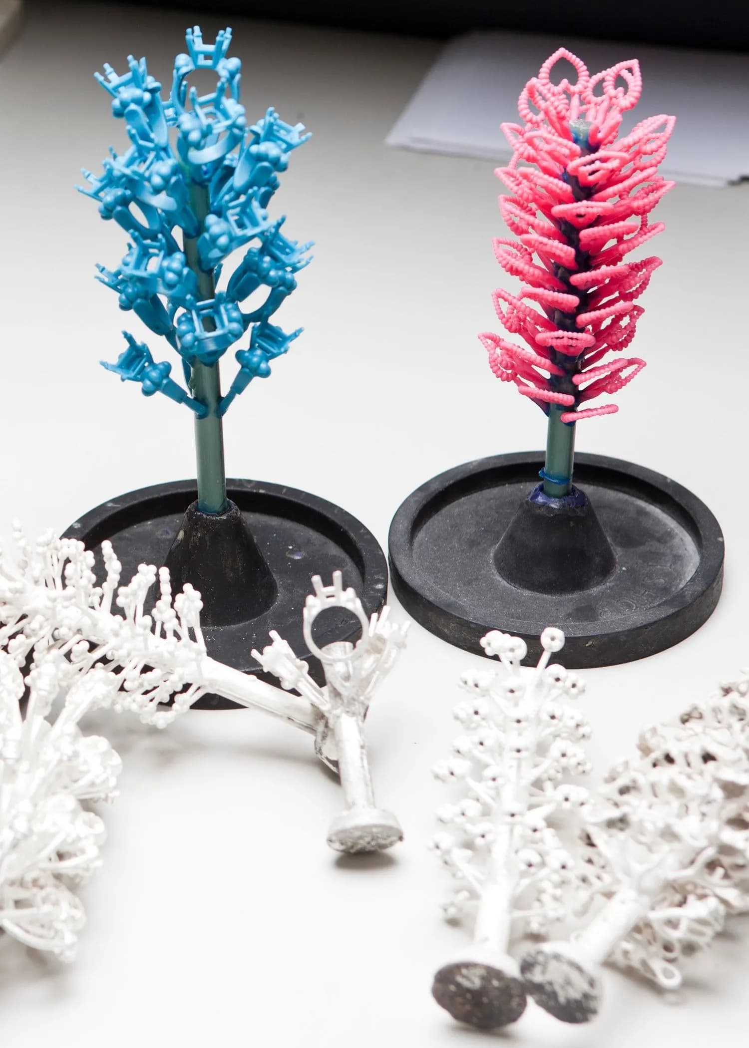 Blue and pink 3D-printed jewellery casting tree with white gold cast rings and sprue system on black investment flasks