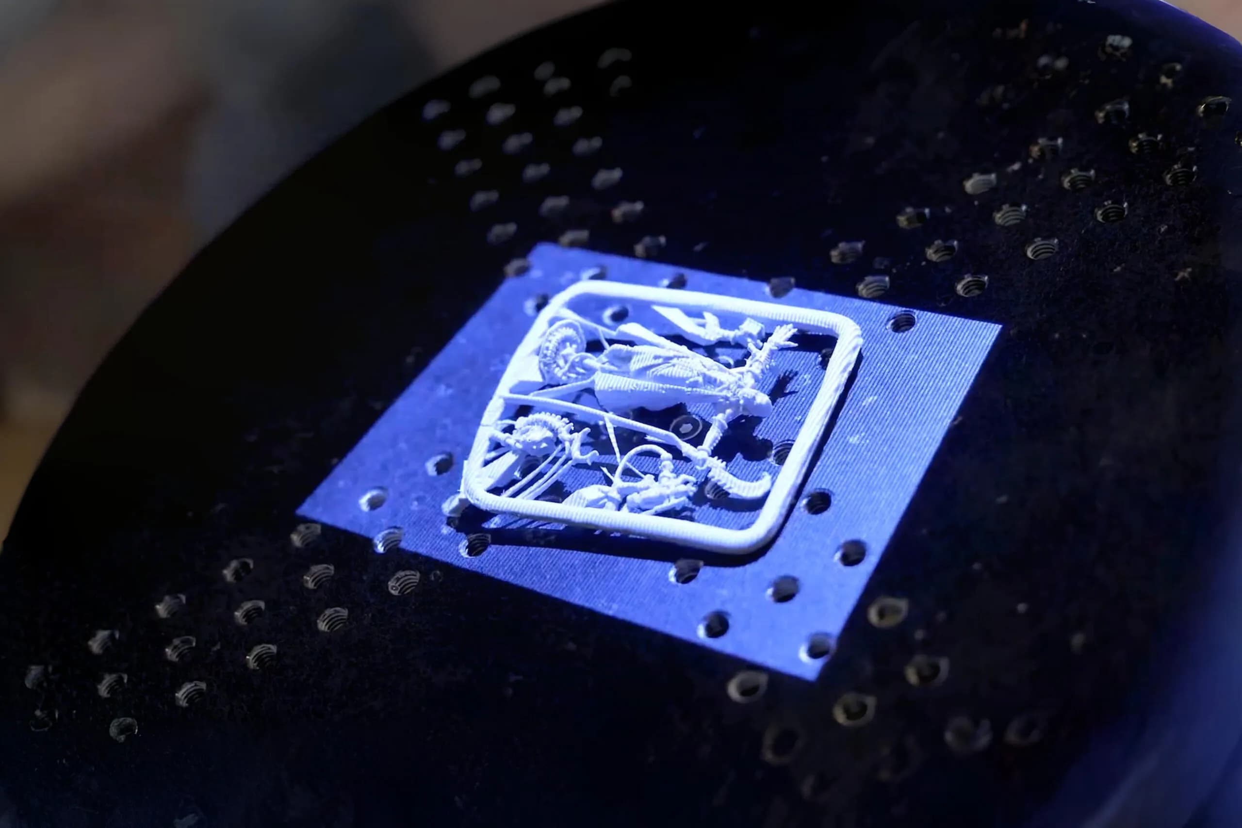 Macro close-up of an intricate resin jewellery pattern printed on a perforated build plate, lit blue