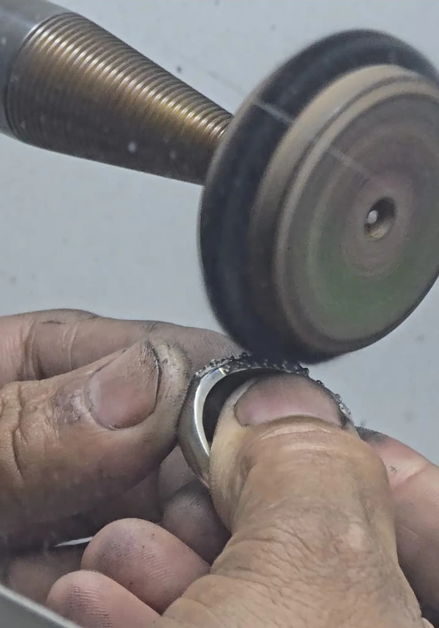 A finisher holding a diamond-set band against a buffing wheel at the polishing bench